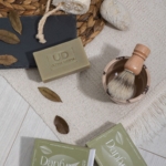 Flat lay του σαπουνιού Daphne με δάφνη, πινέλο ξυρίσματος και κουτιά στο φόντο