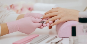 Επαγγελματίας τεχνίτρια νυχιών με ροζ γάντια αποστειρώνει μεταλλικά εργαλεία manicure πάνω σε ροζ στήριγμα χεριού