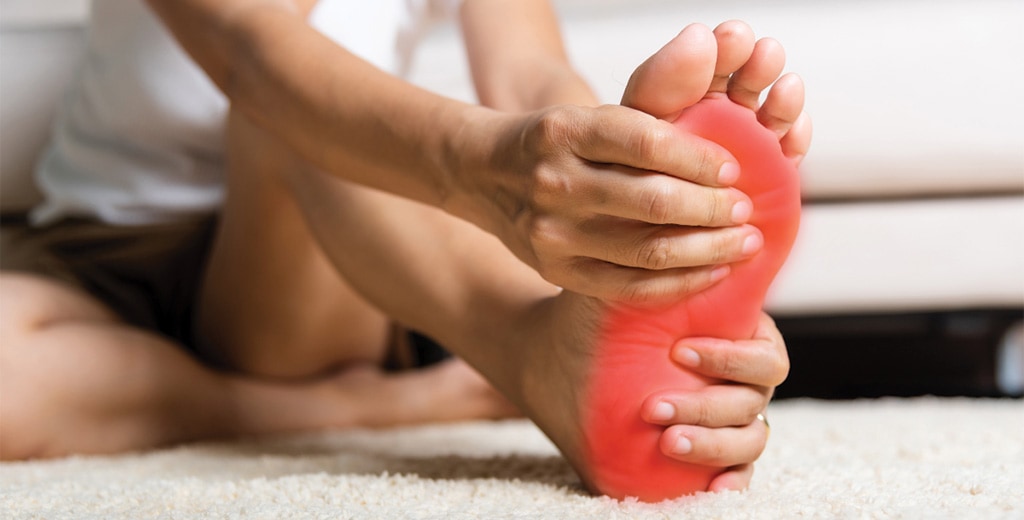 Άτομο κρατά το πέλμα του με εμφανή ερυθρότητα λόγω πόνου, ένδειξη διαβητικού ποδιού