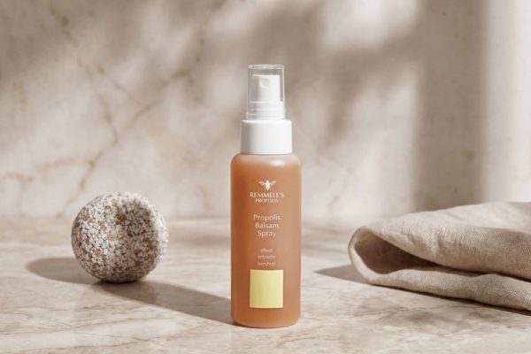 Το Remmele’s Propolis Balsam Spray 80ml τοποθετημένο σε μαρμάρινη επιφάνεια δίπλα σε λινό ύφασμα και διακοσμητική πέτρα.
